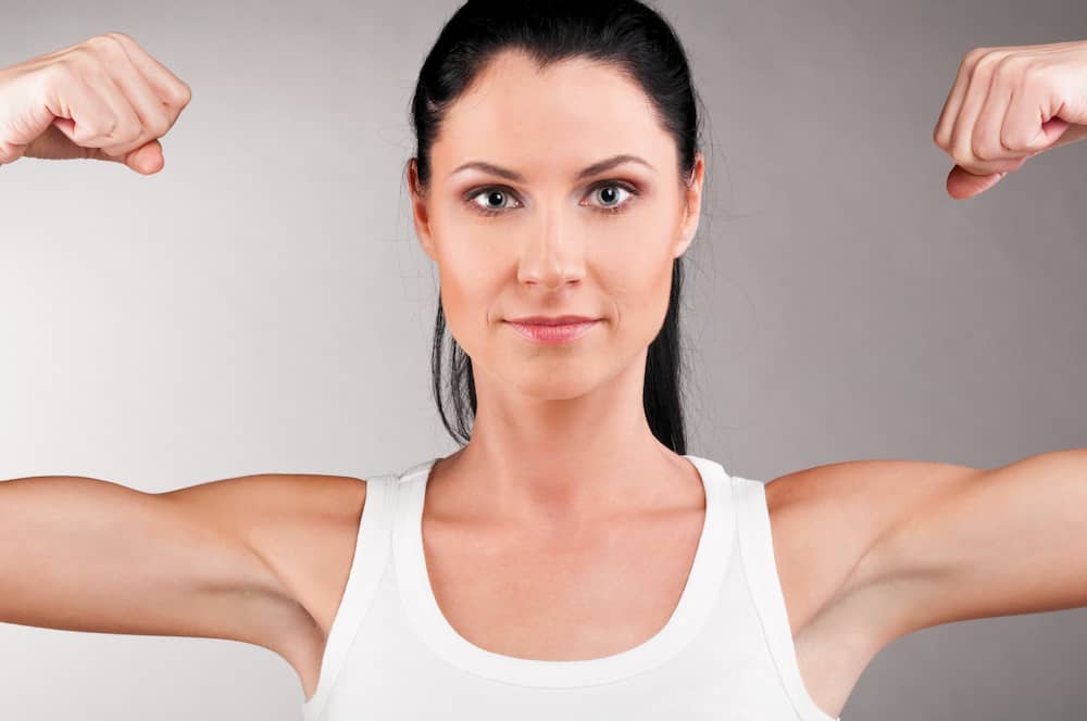 Woman with arms up, flexing arm muscles and neutral facial expression.